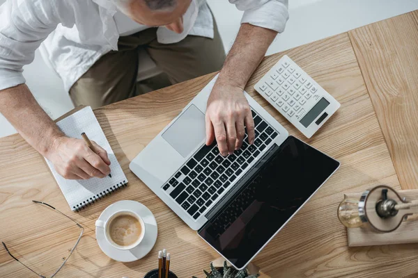 Empresario trabajando en el ordenador portátil y tomando notas - foto de stock