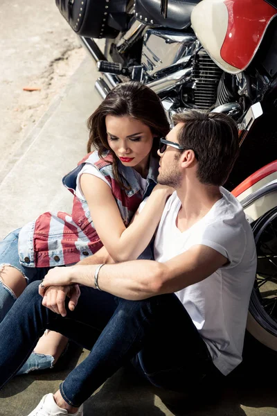Joven elegante pareja sentado cerca de la motocicleta - foto de stock