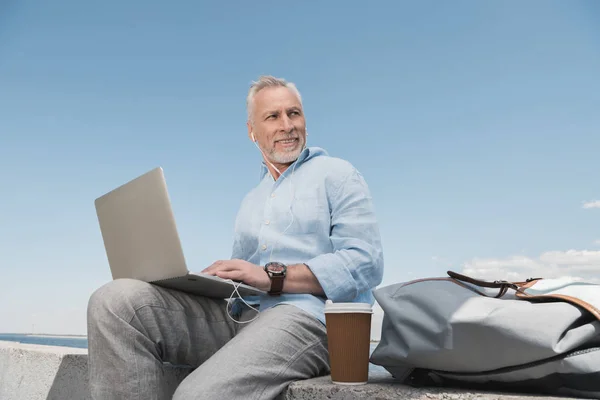 Senior man using laptop at quay — Stock Photo