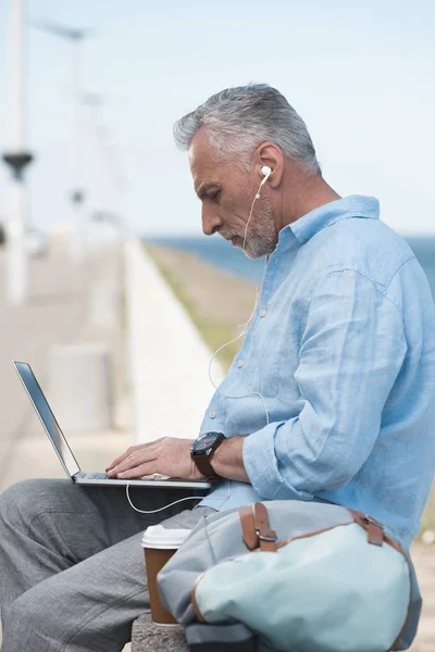 Elderly man typing on laptop outdoors — Stock Photo