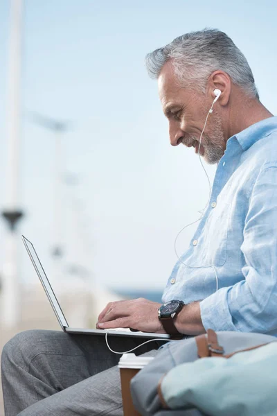 Hombre mayor que trabaja en el ordenador portátil al aire libre - foto de stock