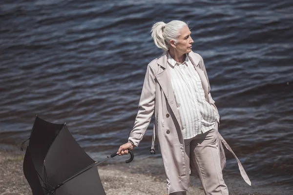 Woman walking with umbrella on river shore — Stock Photo