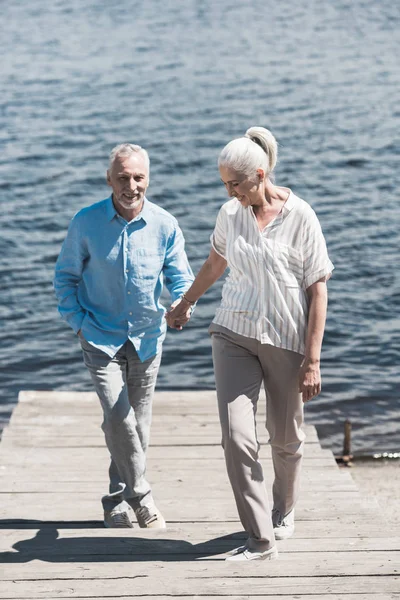 Sonriente pareja de ancianos caminando a orillas del río - foto de stock