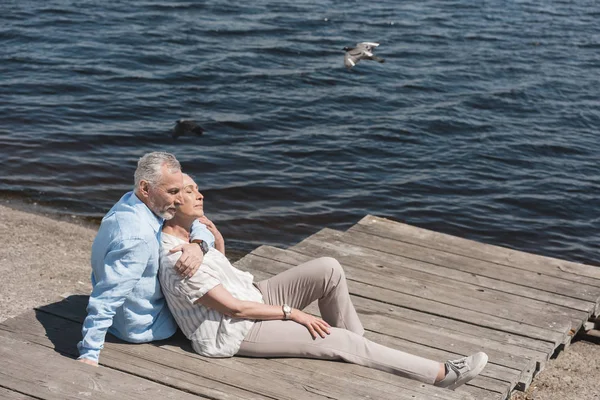 Casual pareja de ancianos relajándose a orillas del río - foto de stock