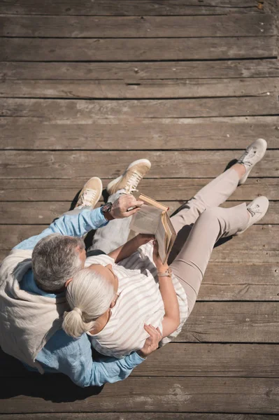 Senior couple reading book on pavement — Stock Photo