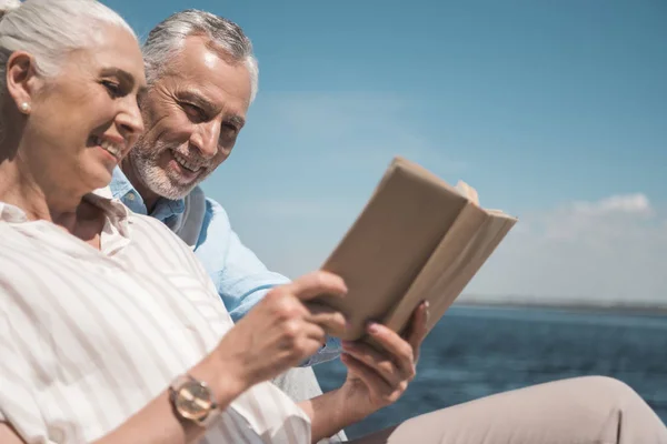 Elderly couple reading book on quay — Stock Photo