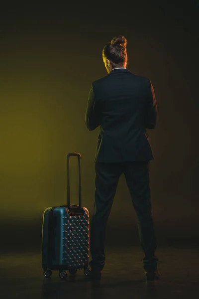 Молодой человек в костюме стоит рядом с чемоданом — стоковое фото
