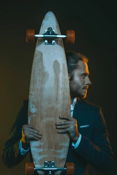 Jeune homme en costume tenant skateboard — Photo de stock