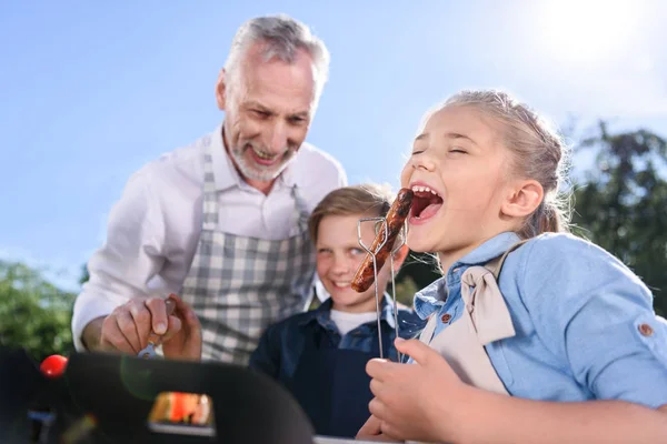 Petits-enfants avec grand-père manger des saucisses sur le pique-nique — Photo de stock