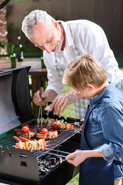Abuelo con nieto preparando carne a la parrilla - foto de stock