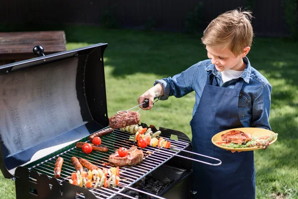 Kid boy preparing stakes on grill — Stock Photo