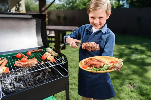 Kid boy preparing stakes on grill — Stock Photo