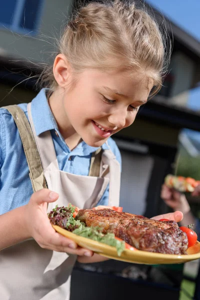 Criança menina segurando prato com bife — Fotografia de Stock