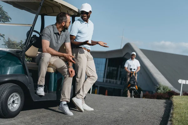 Amigos hablando mientras están sentados en el carrito de golf - foto de stock