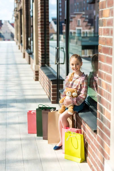 Girl with shopping bags holding teddy bear — Stock Photo