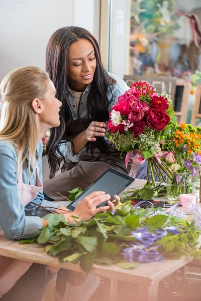 Floristas multiétnicos com tablet digital e flores — Fotografia de Stock