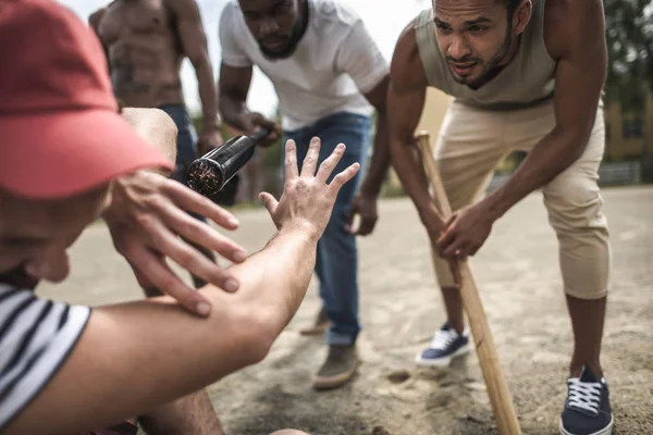 Hombres atacando a otro con bates de béisbol - foto de stock