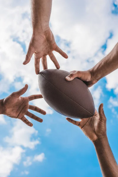 Mani che tengono palla da football americano — Foto stock