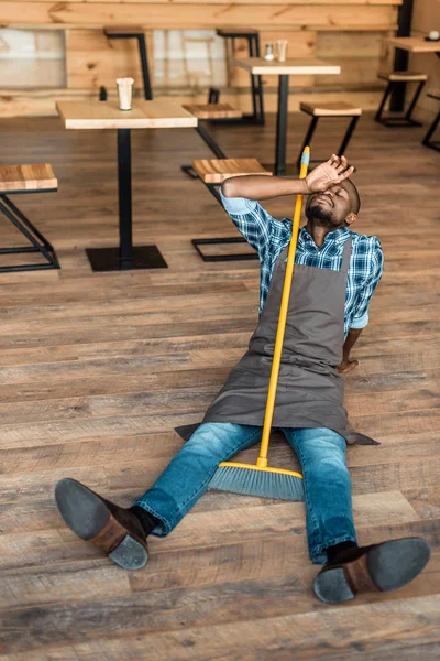 Homem cansado no chão com vassoura — Fotografia de Stock