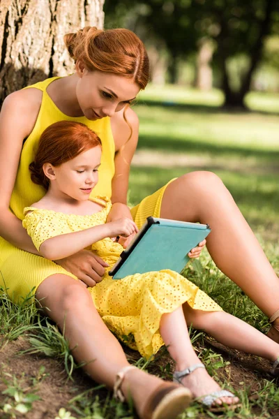 Madre e hija con gadget en el parque - foto de stock