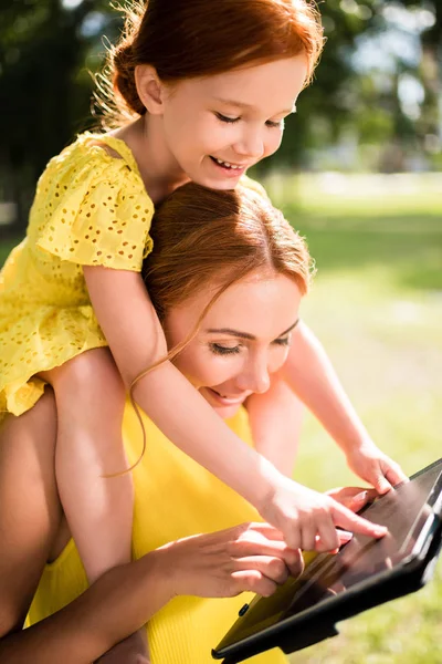 Madre e hija con gadget en el parque - foto de stock