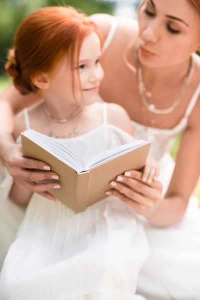 Madre e hija con libro en el parque - foto de stock