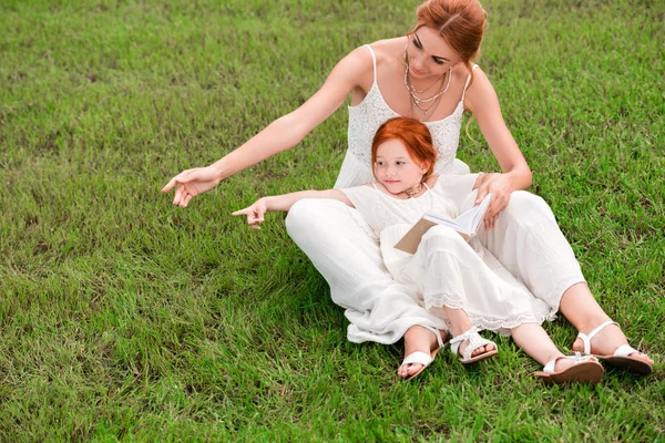 Madre e hija con libro en el parque - foto de stock