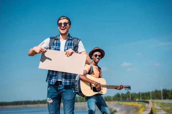 Multiethnic men with empty cardboard hitchhiking — Stock Photo