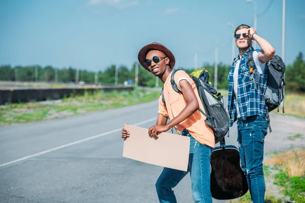 Multiethnic men with cardboard hitchhiking — Stock Photo