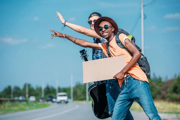 Multiethnic men with cardboard hitchhiking — Stock Photo