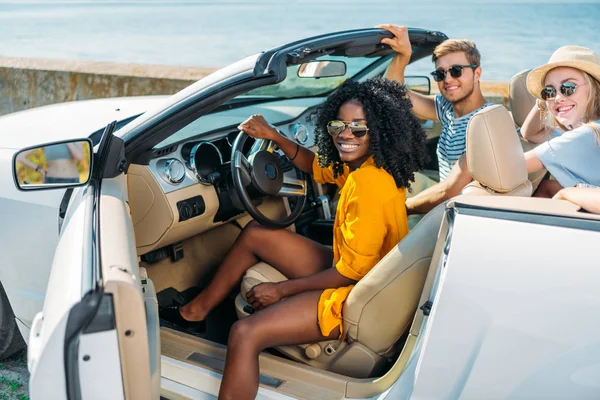 Multicultural friends riding car at seaside — Stock Photo
