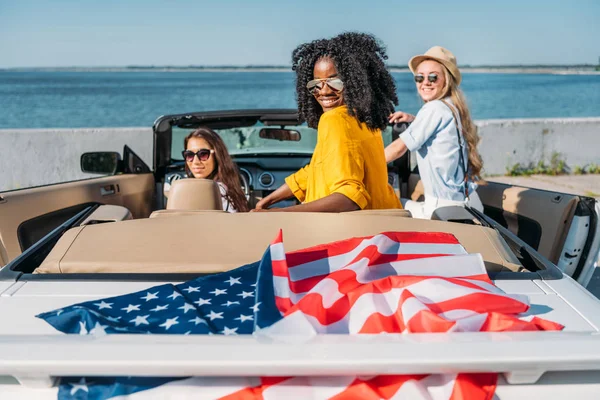 Mujeres multiétnicas en coche con bandera americana - foto de stock