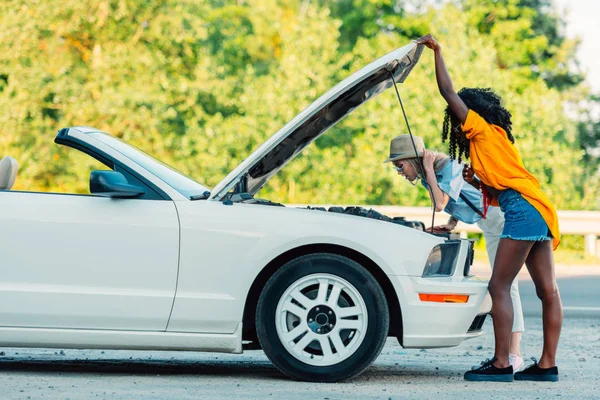 Mujeres multiétnicas de pie cerca de coche roto - foto de stock