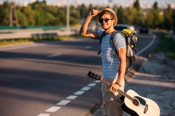 Man with guitar hitchhiking alone — Stock Photo