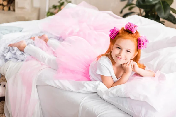 Petite fille avec des bigoudis reposant sur le lit — Photo de stock