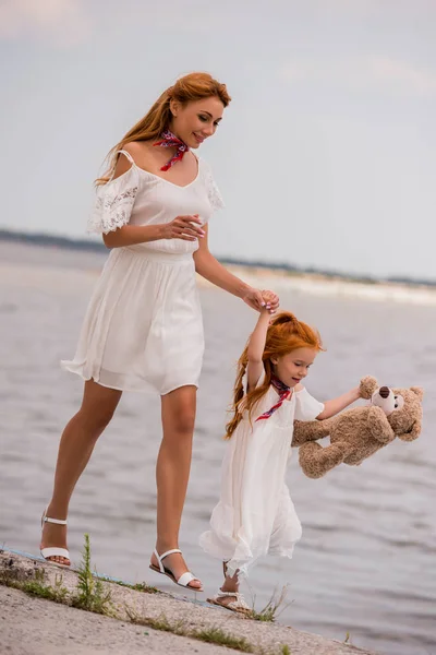 Madre e hija con osito de peluche en la orilla del mar - foto de stock