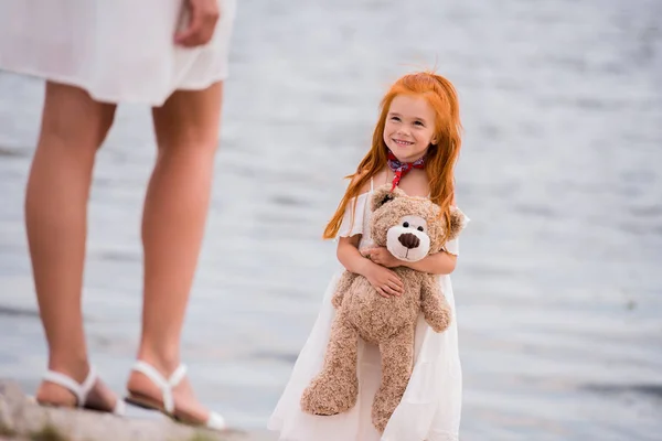 Mother and daughter with teddy bear at seashore — Stock Photo