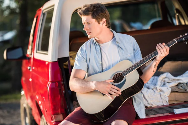 Uomo che suona la chitarra sul bagagliaio auto — Foto stock