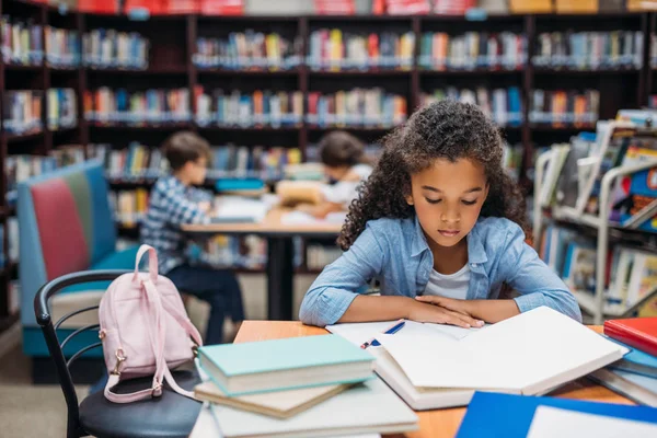 Schoolgirl reading book in library — Stock Photo