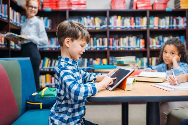 Schoolboy using tablet at library — Stock Photo