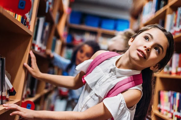 Школярки шукають книги в бібліотеці — стокове фото