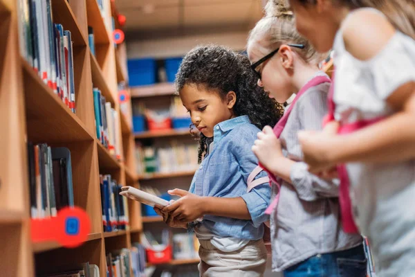 Schoolgirls looking for books in library — Stock Photo