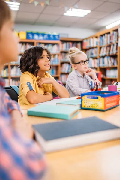 Niños sentados en el escritorio en la biblioteca - foto de stock