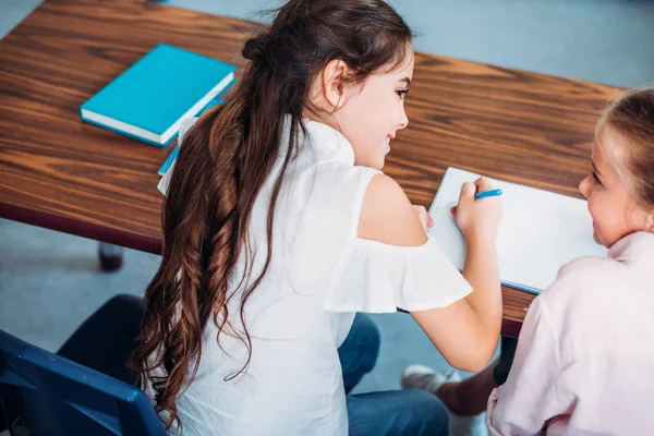 Colegialas hablando mientras está sentado en el escritorio - foto de stock