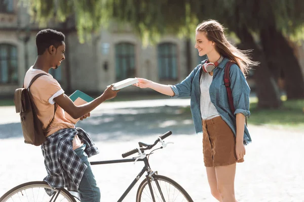 Pareja multiétnica con libros y bicicleta - foto de stock