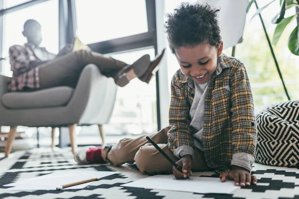 Niño dibujo mientras padre sentado en sillón - foto de stock