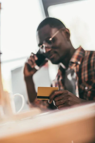 Мужчина с кредитной картой разговаривает на смартфоне — стоковое фото