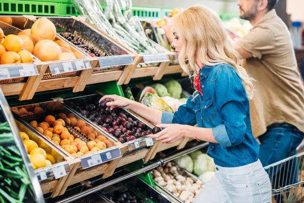 Woman choosing plums in grocery shop — Stock Photo