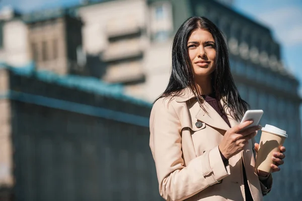 Woman in trench coat with smartphone — Stock Photo