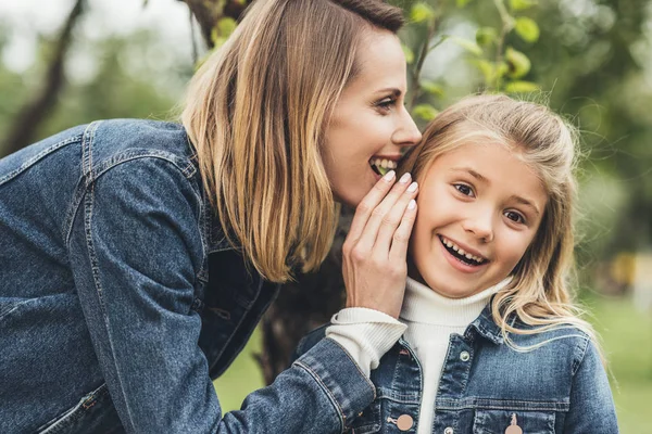 Madre susurrando a su hija - foto de stock